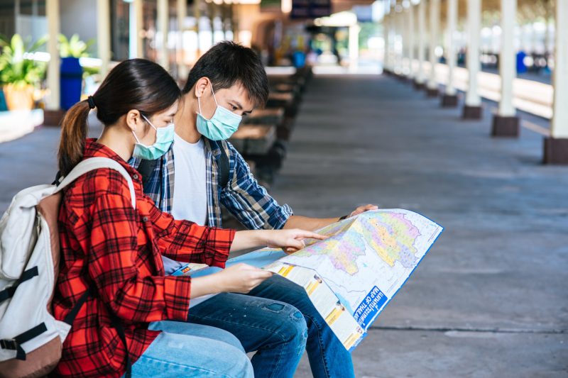 Male and female tourists look at the map beside the railway.